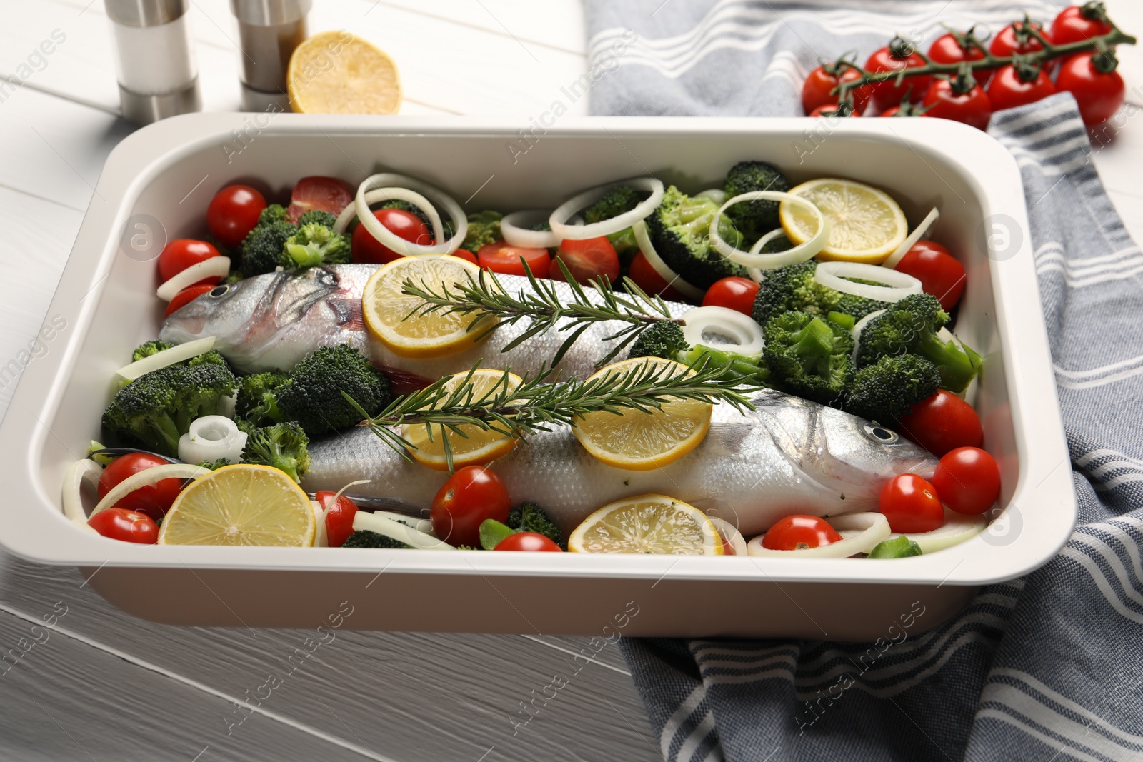 Photo of Raw fish with vegetables and lemon in baking dish on white wooden table