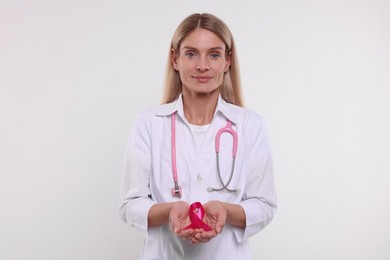 Doctor with stethoscope holding pink ribbon on white background. Breast cancer awareness