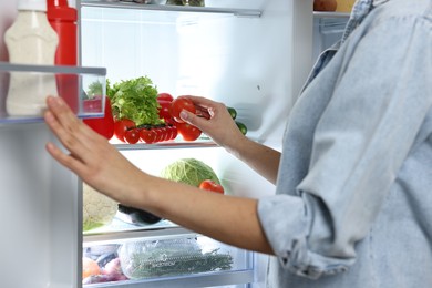 Photo of Young woman taking tomato out of refrigerator, closeup