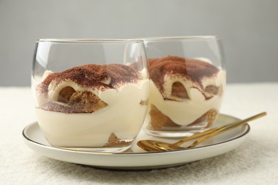 Delicious tiramisu in glasses and spoons on white table, closeup