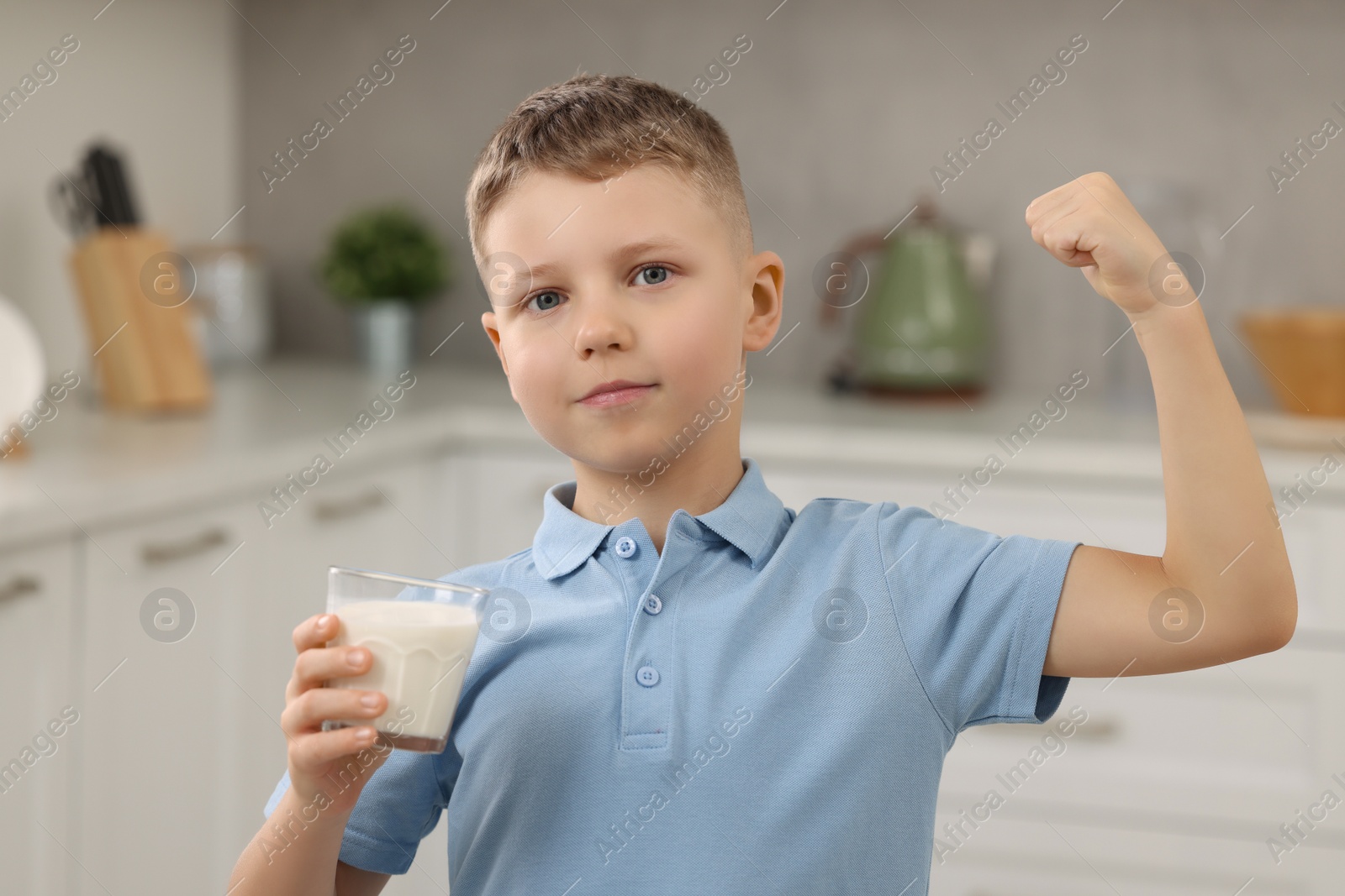 Photo of Cute boy with glass of fresh milk showing his strength in kitchen