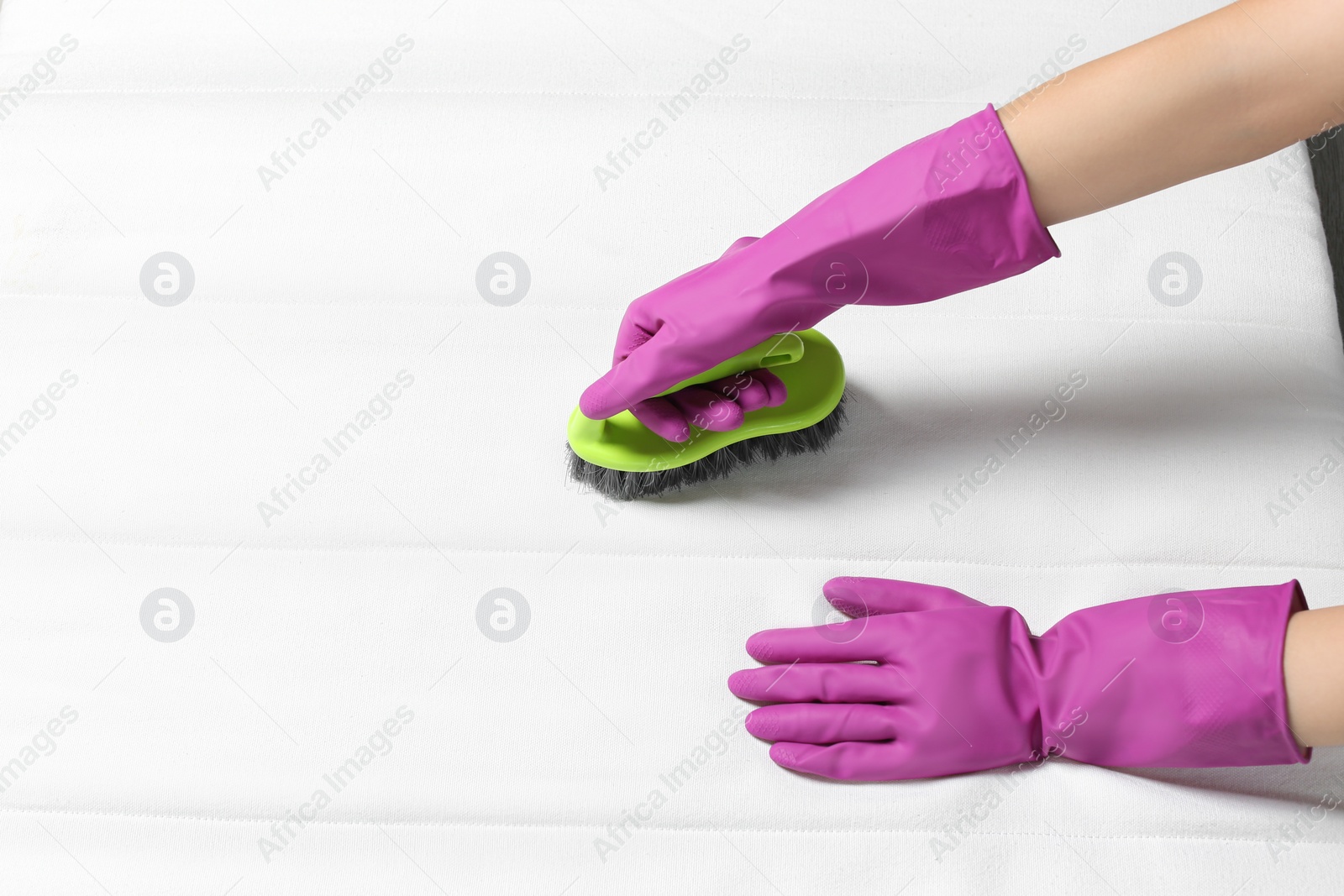 Photo of Woman in purple gloves cleaning white mattress with brush, closeup. Space for text