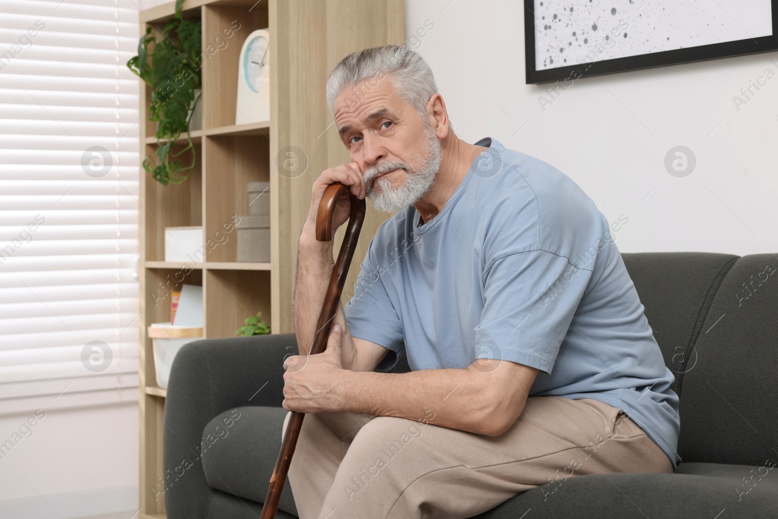 Photo of Senior man with walking cane sitting on sofa at home