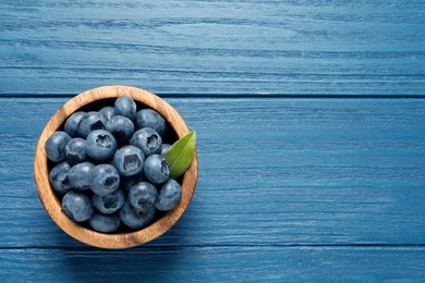 Photo of Bowl of fresh tasty blueberries on blue wooden table, top view. Space for text