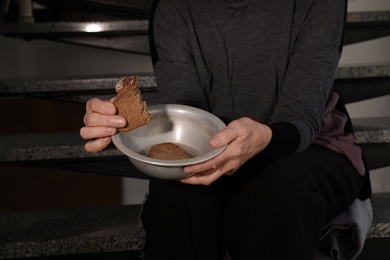 Photo of Poor mature woman with bowl and bread on stairs, closeup