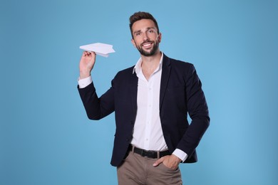 Photo of Handsome businessman playing with paper plane on light blue background