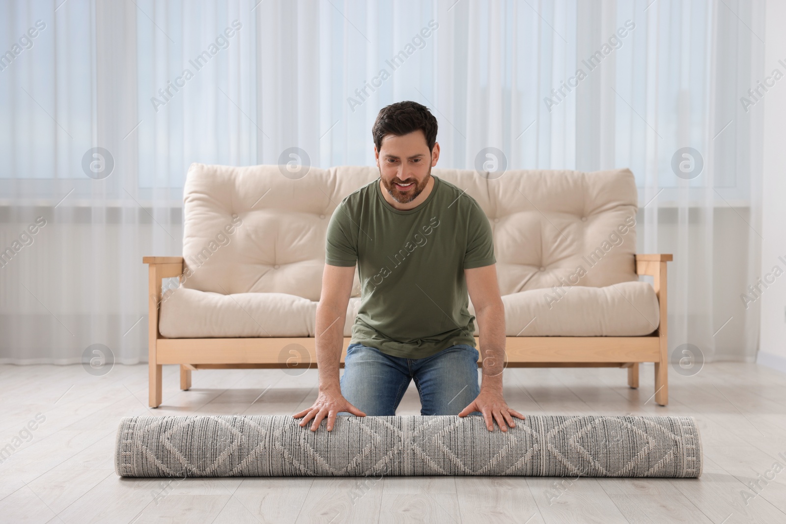 Photo of Smiling man unrolling carpet with beautiful pattern on floor in room