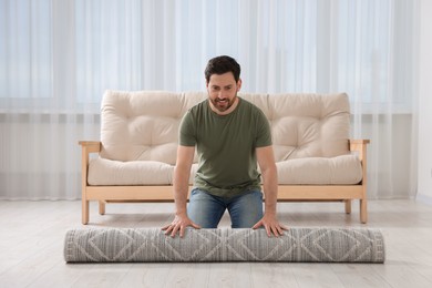 Smiling man unrolling carpet with beautiful pattern on floor in room