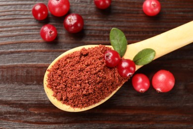 Photo of Dried cranberry powder in spoon, fresh berries and green leaves on wooden table, top view