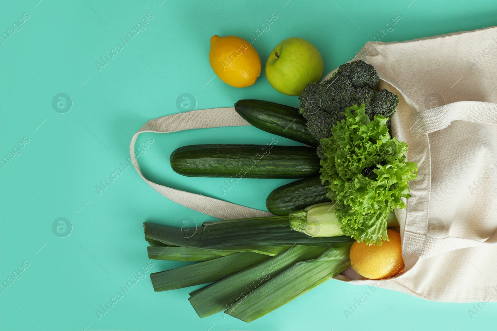 Photo of Net bag with fruits and vegetables on turquoise background, flat lay