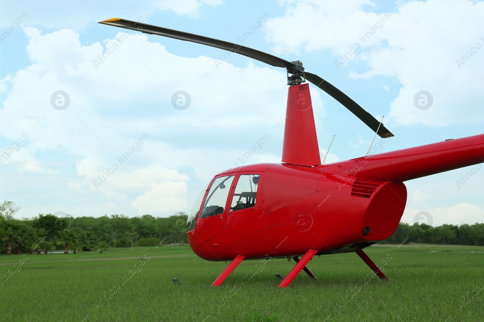 Photo of Modern red helicopter on green grass outdoors