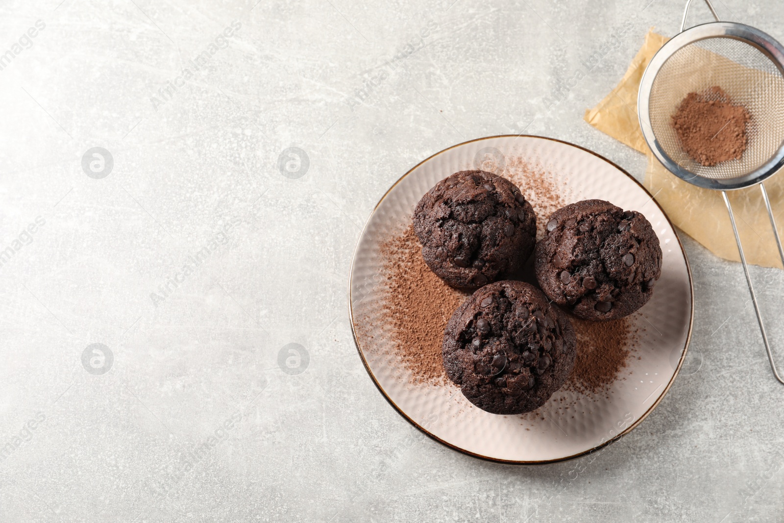 Photo of Delicious chocolate muffins and cacao powder on light grey table, flat lay. Space for text