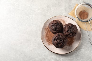 Delicious chocolate muffins and cacao powder on light grey table, flat lay. Space for text