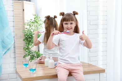 Photo of Little girl brushing teeth in bathroom at home