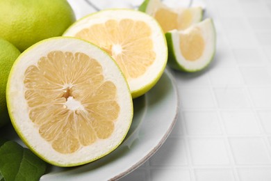 Whole and cut sweetie fruits on white tiled table, closeup. Space for text