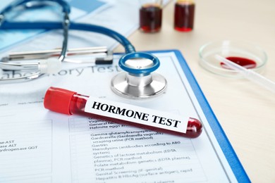 Photo of Hormone test. Sample tube with blood, stethoscope and laboratory form on table, closeup
