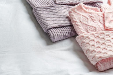 Photo of Stylish knitted sweaters on white fabric, closeup