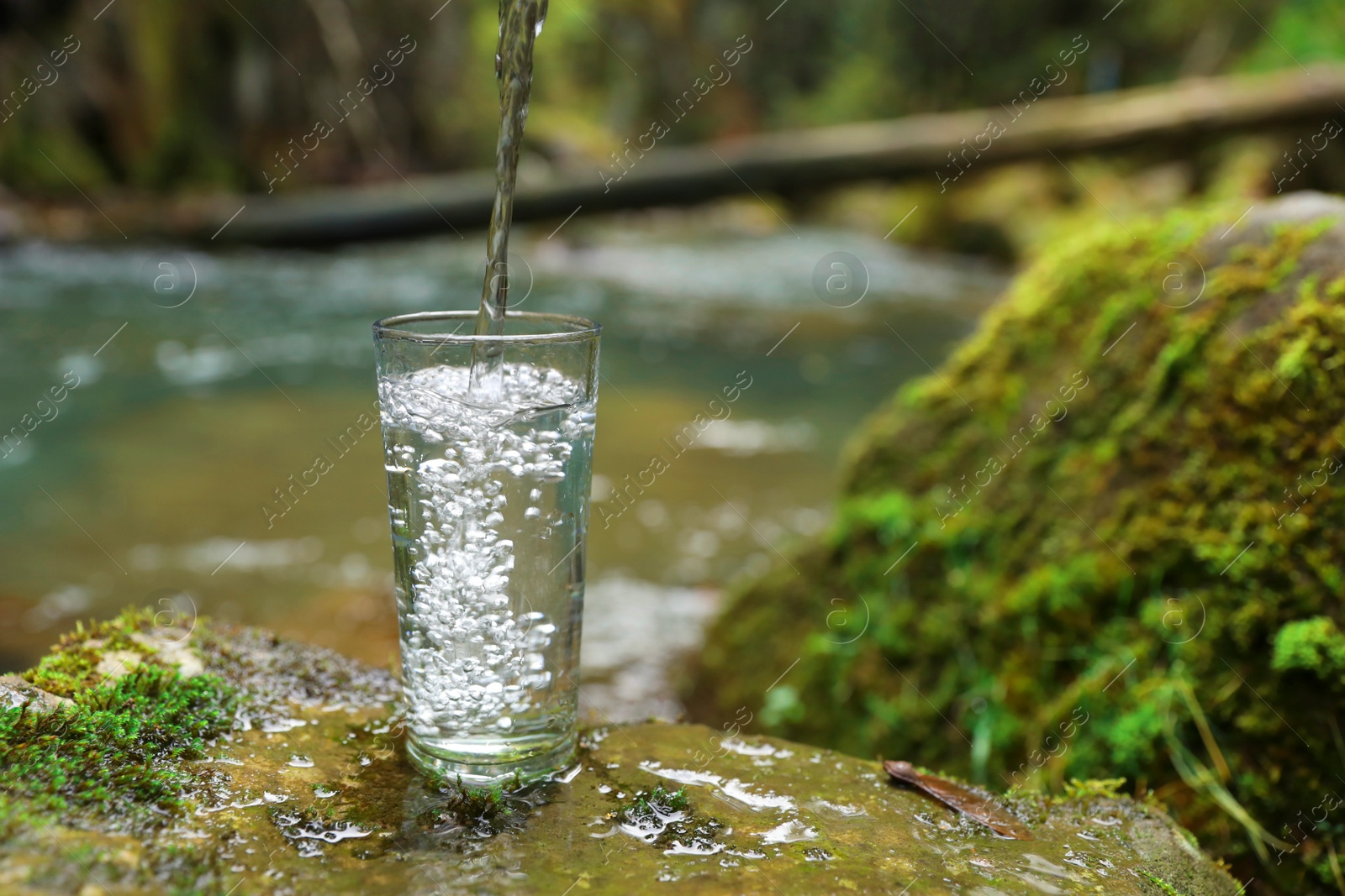 Photo of Fresh water pouring into glass on stone with moss near river. Space for text