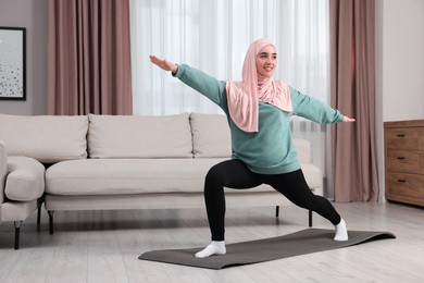Photo of Muslim woman in hijab doing exercise on fitness mat at home. Space for text