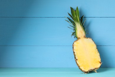 Photo of Half of ripe juicy pineapple on light blue wooden table, space for text