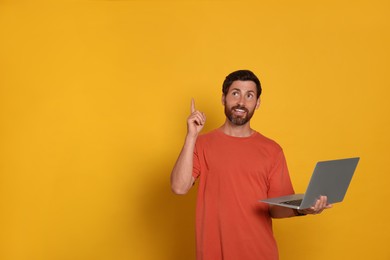 Photo of Handsome man with laptop on orange background