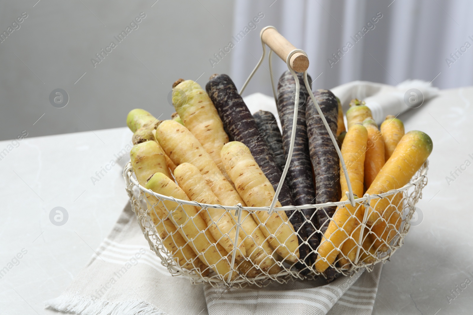 Photo of Many different raw carrots in metal basket on table