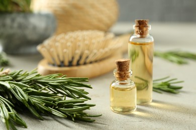 Photo of Essential oil in bottles and rosemary on light gray table, closeup