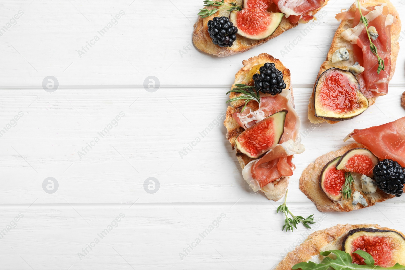 Photo of Sandwiches with ripe figs and prosciutto served on white wooden table, flat lay. Space for text