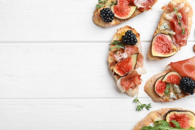 Sandwiches with ripe figs and prosciutto served on white wooden table, flat lay. Space for text