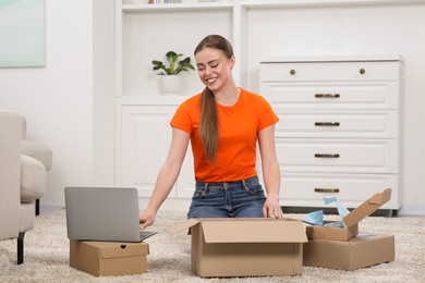 Happy woman with laptop unpacking parcels at home. Online store