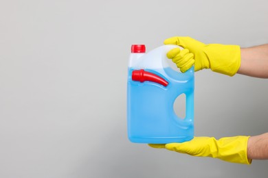 Photo of Man in rubber gloves holding canister with blue liquid on light grey background, closeup. Space for text