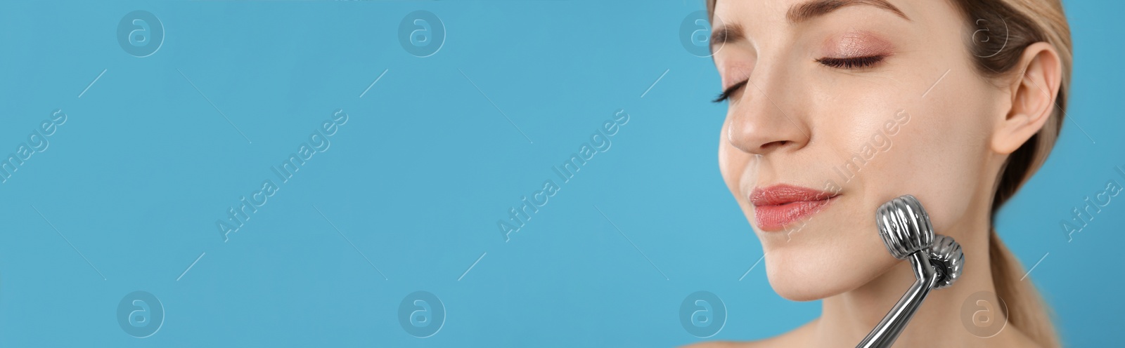 Image of Young woman using metal face roller on light blue background, space for text. Banner design