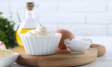 Photo of Fresh mayonnaise sauce in bowl and ingredients on table