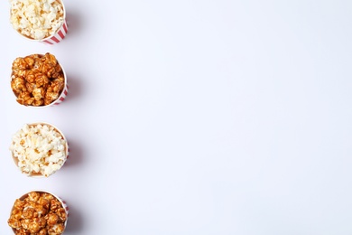 Photo of Different kinds of popcorn in paper cups on white background, top view. Space for text