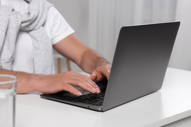 Photo of Man using laptop at white table indoors, closeup