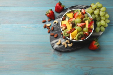 Photo of Tasty fruit salad in bowl and ingredients on light blue wooden table, flat lay. Space for text