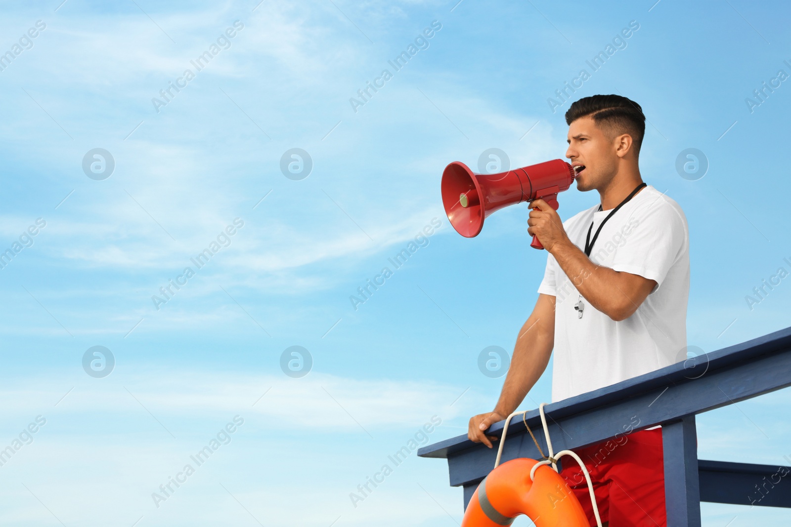 Photo of Male lifeguard with megaphone on watch tower against blue sky