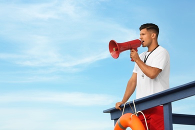 Photo of Male lifeguard with megaphone on watch tower against blue sky