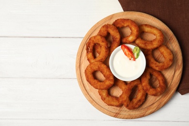 Wooden board with tasty onion rings and sauce on table, top view