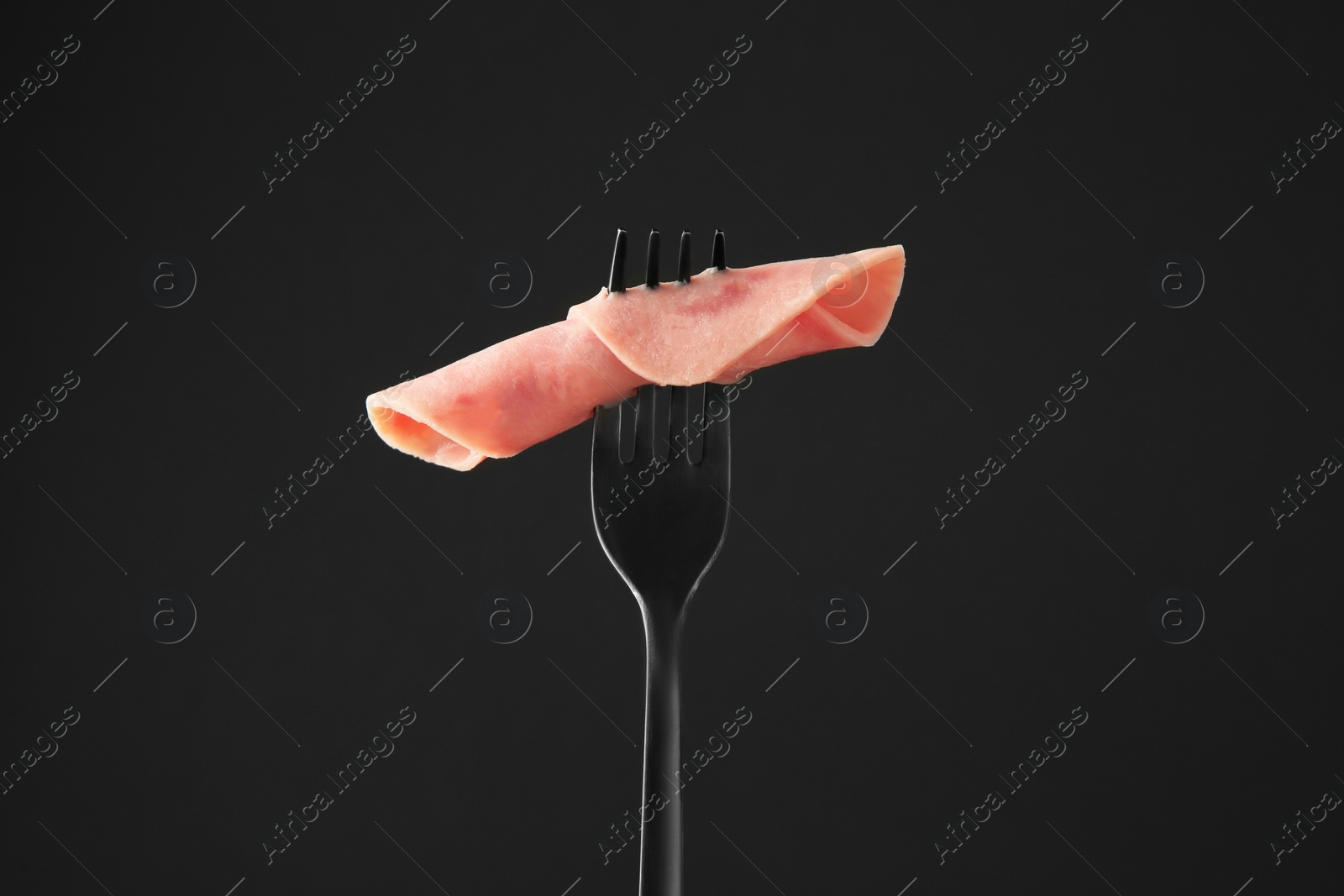 Photo of Fork with tasty slice of ham on black background