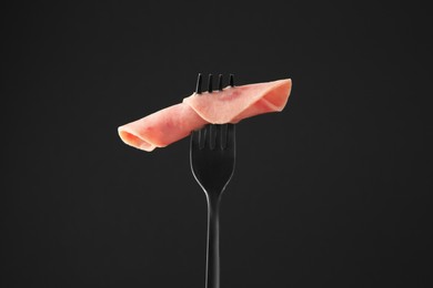 Photo of Fork with tasty slice of ham on black background