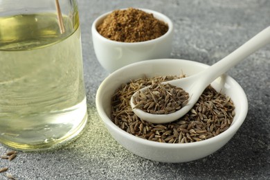 Photo of Caraway (Persian cumin) seeds, powder and oil on gray textured table, closeup