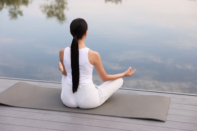 Photo of Woman practicing Padmasana on yoga mat outdoors, back view. Lotus pose