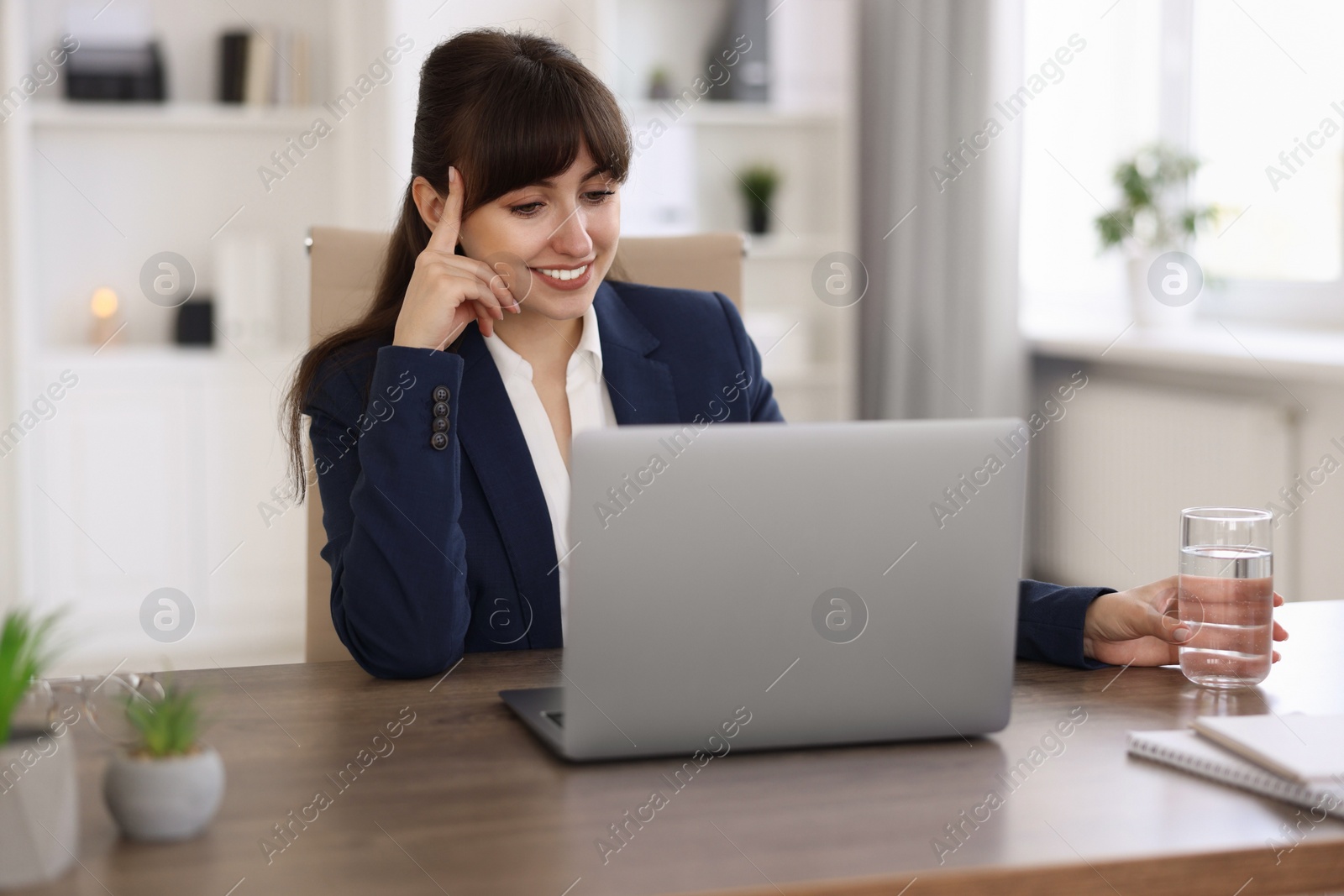 Photo of Woman with glass of water watching webinar at wooden table in office