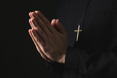 Photo of Priest in cassock praying on dark background, closeup