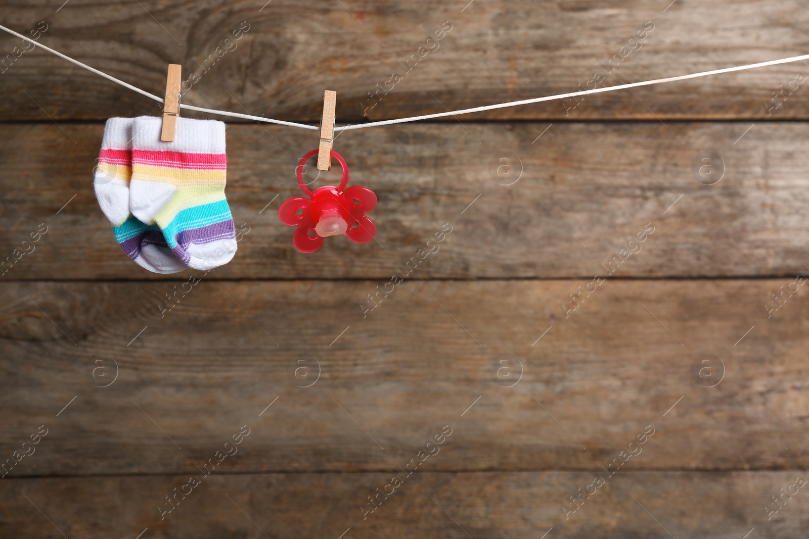 Photo of Pair of socks and pacifier on laundry line against wooden background, space for text. Baby accessories