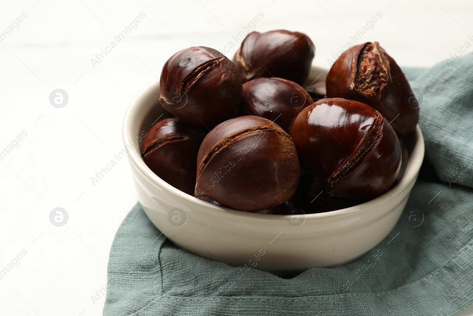 Photo of Roasted edible sweet chestnuts in bowl on white table, closeup