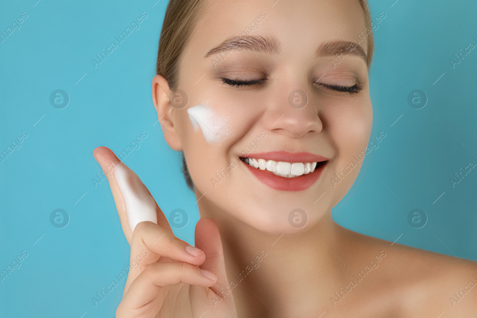 Photo of Young woman washing face with cleansing foam on light blue background. Cosmetic product