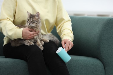 Photo of Pet shedding. Woman with lint roller removing cat`s hair from trousers on sofa at home, closeup