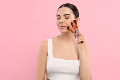 Photo of Beautiful woman with different makeup brushes on pink background